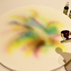 Roll out the remaining white Renshaw extra sugarpaste and cover a 16 inch round cake board. Spray on various rainbow colours with an airgun making an outward rainbow splash effect using Rainbowdust (colour Flo) airbrush colours. Leave board set and dry before attaching the boot.