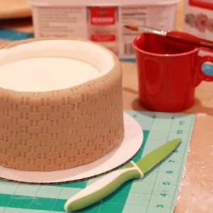 For the middle tier, use the basket weave impression pin. Use a mixture of ivory and brown fondant again but a shade darker than the bottom tier. Use a panelling technique to apply.