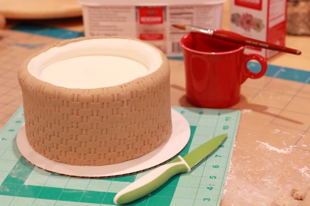 For the middle tier, use the basket weave impression pin. Use a mixture of ivory and brown fondant again but a shade darker than the bottom tier. Use a panelling technique to apply.