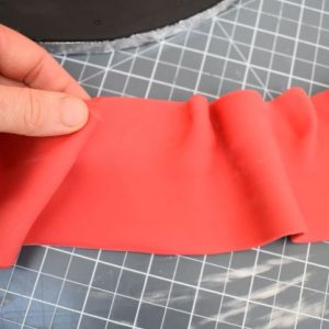 Add a teaspoon of tylose powder to the remaining red sugarpaste and knead. This will strengthen the paste and help it to hold the shape of the brim. Roll out the red sugarpaste into a long strip and pinch one side in random spots to create ruffles in the brim.