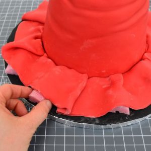 Attach the brim around the base of the hat using edible glue. To create a little movement, place pieces of foam under some sections of the brim as shown. These can be removed once the brim dries.