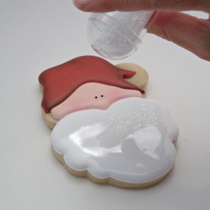Fill Santa’s beard with white flood icing. Quickly pop any air bubbles and smooth out the icing. While it is still wet, sprinkle the surface with gold iridescent Disco Dust.