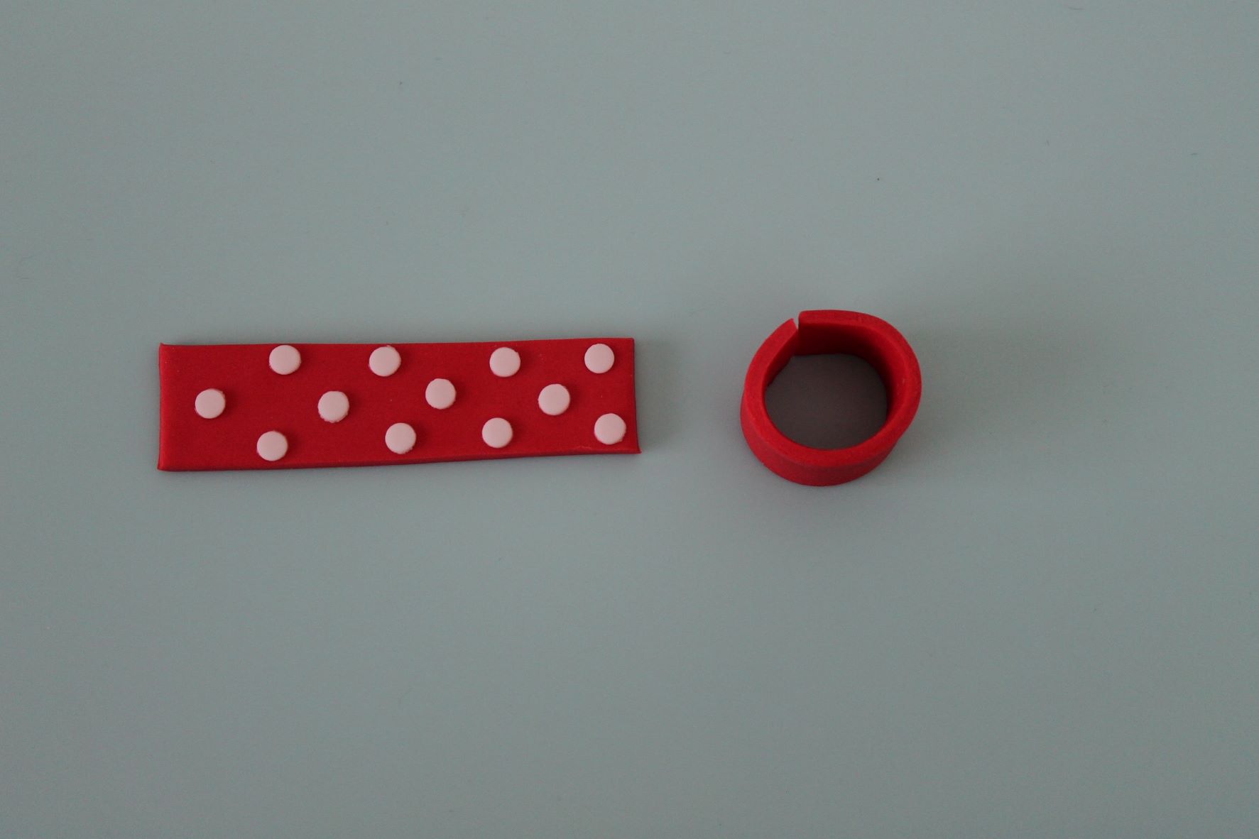 To make the present, colour a small amount of modelling paste red and roll it out to a couple of millimetres thick. Using a small round plunger cutter, cut out circles of thinly rolled white modelling paste and stick onto the red strip. Curl the strip to create a cylinder. Roll a thicker piece of red and cut a larger circle out for the present lid. Cover in white dots to match the present.